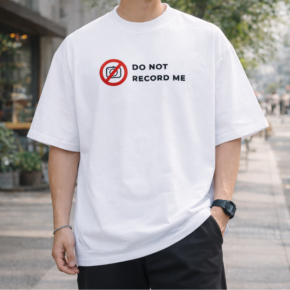 Person wearing a white t-shirt with 'Do Not Record Me' graphic outdoors.